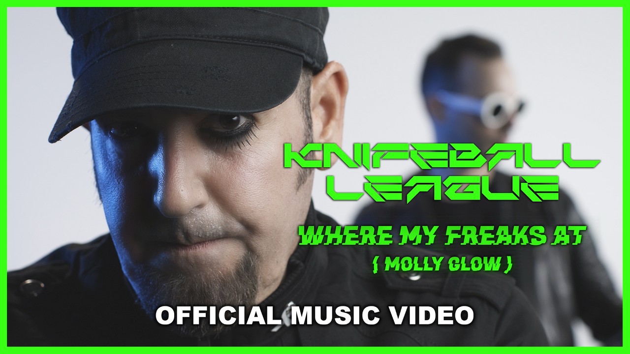 Knifeball League — a close-up of a man with a goatee in a dark military cap, lit blue down one side, with a second band member out of focus behind him in round white goggles. Green lettering reads Knifeball League, Where My Freaks At (Molly Glow), the bottom edge is marked Official Music Video, and the whole frame has a bright green border.